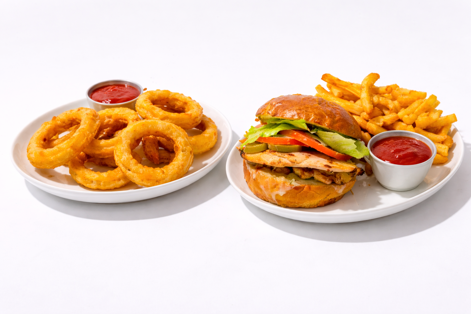 Plates of onion rings and a chicken sandwich with fries, served with ketchup.