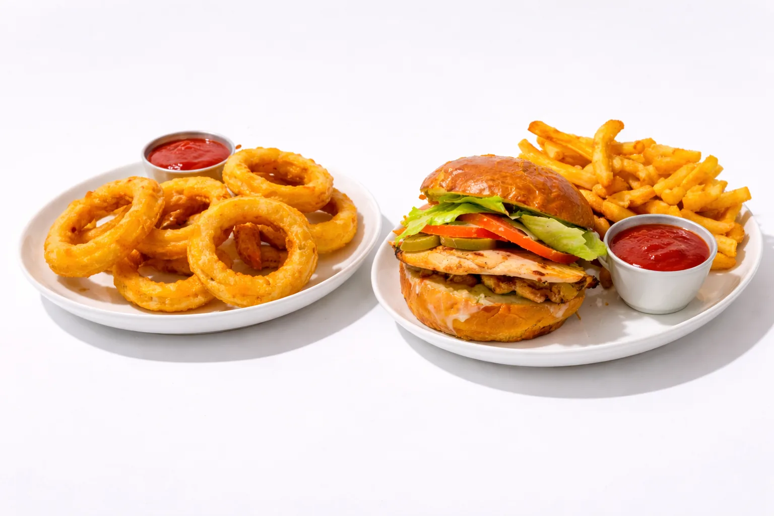 Plates of onion rings and a chicken sandwich with fries, served with ketchup.