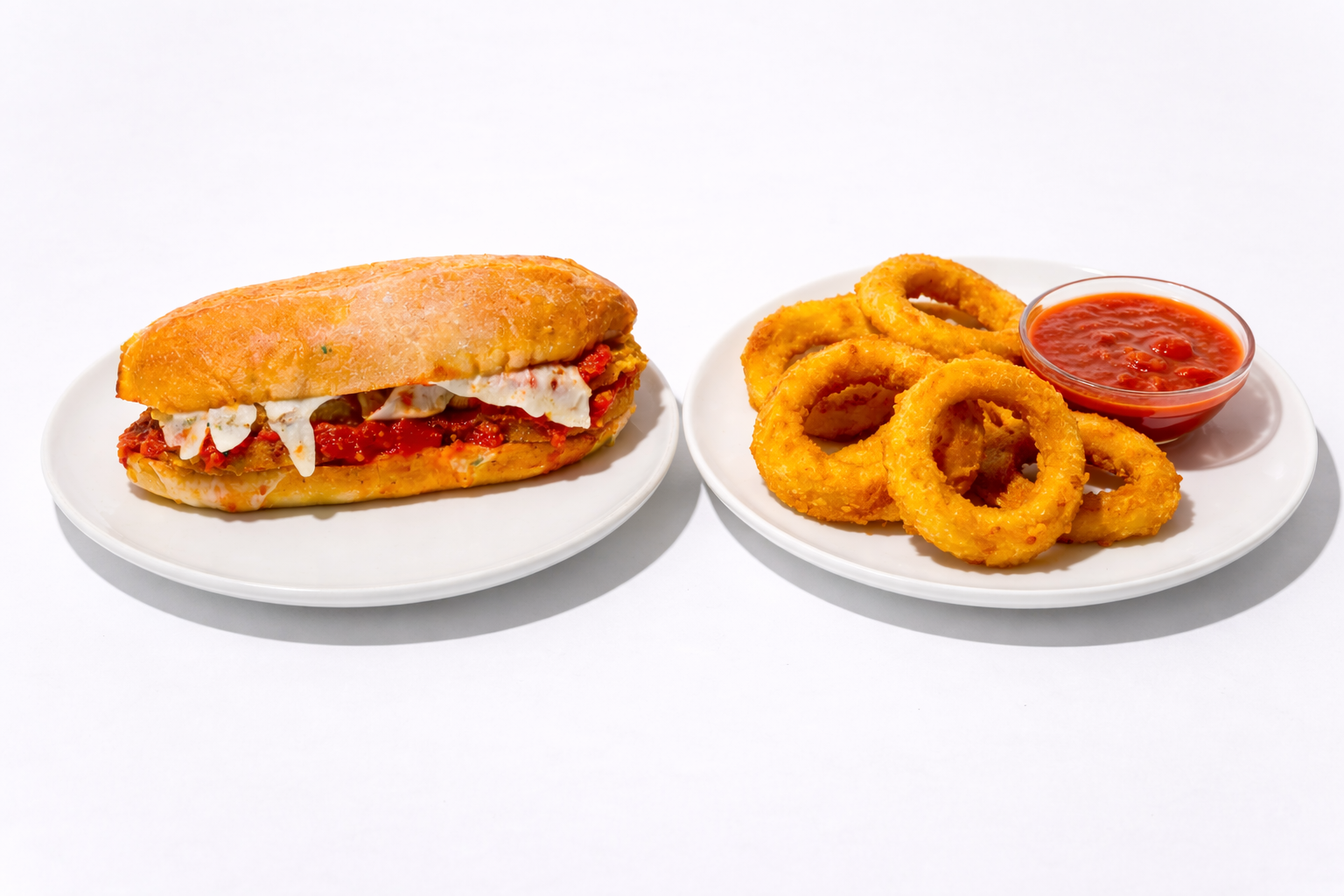 Sandwich on a plate with a side of onion rings and marinara sauce.