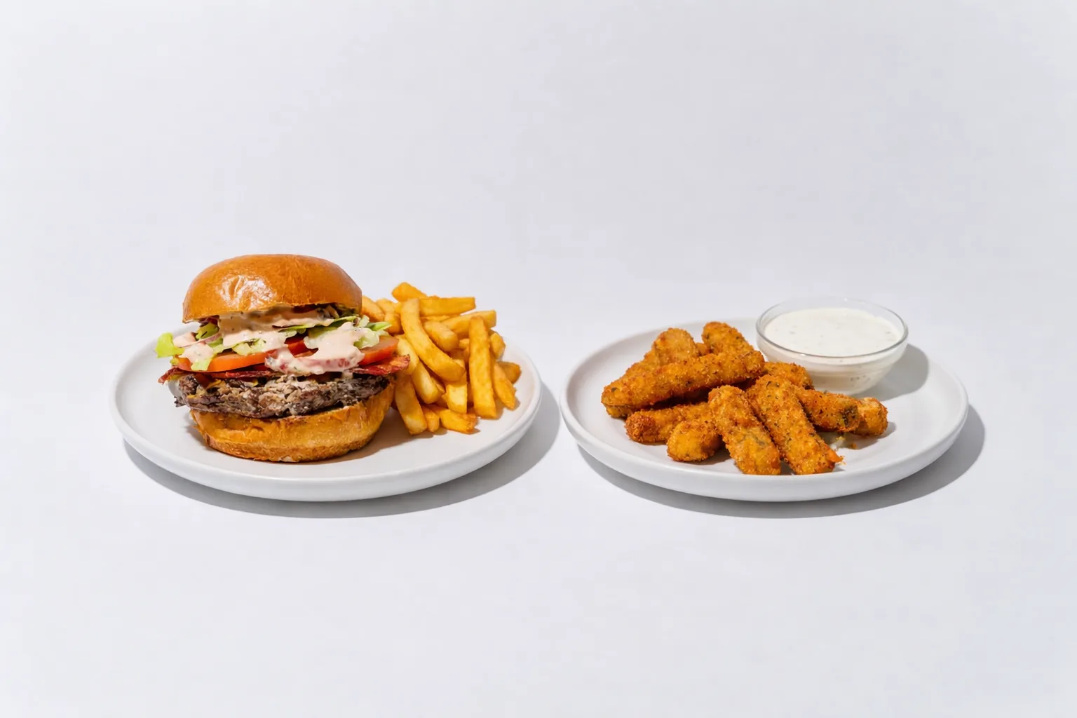 Burger with fries on one plate and breaded bites with dipping sauce on another.